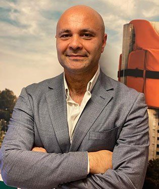 Uomo sorridente con le braccia incrociate e giacca azzurra. Sullo sfondo un salvagente.