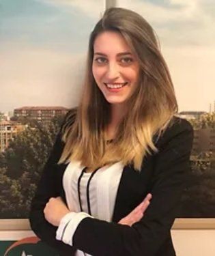 Donna con le braccia incrociate, sorridente, che indossa un blazer nero e un top bianco, davanti a una finestra.