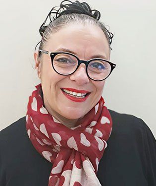 Donna sorridente con occhiali e sciarpa rossa.