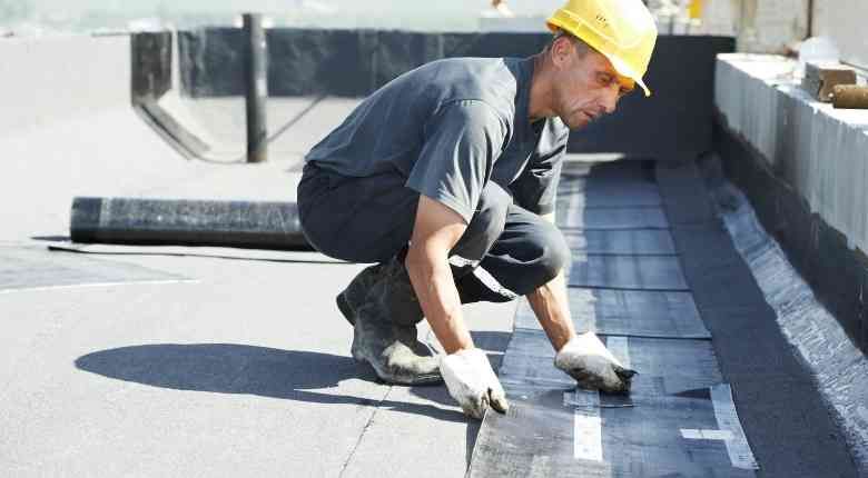 A man wearing a hard hat is working on a roof.