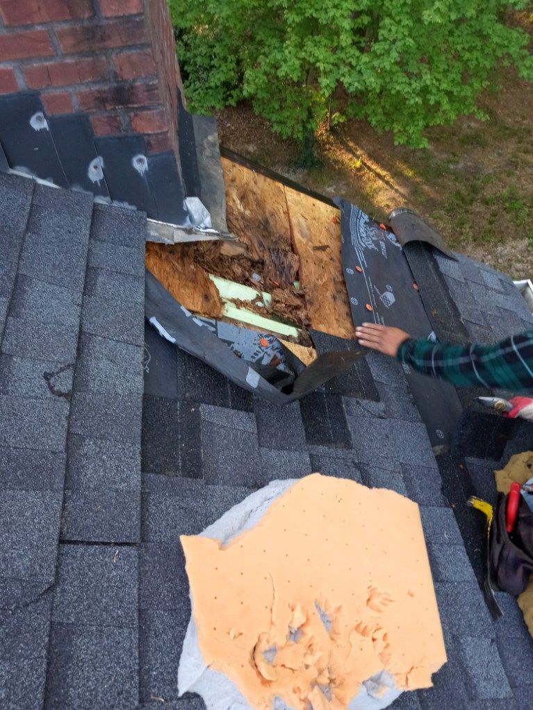 A person is working on a roof with a brick chimney in the background.