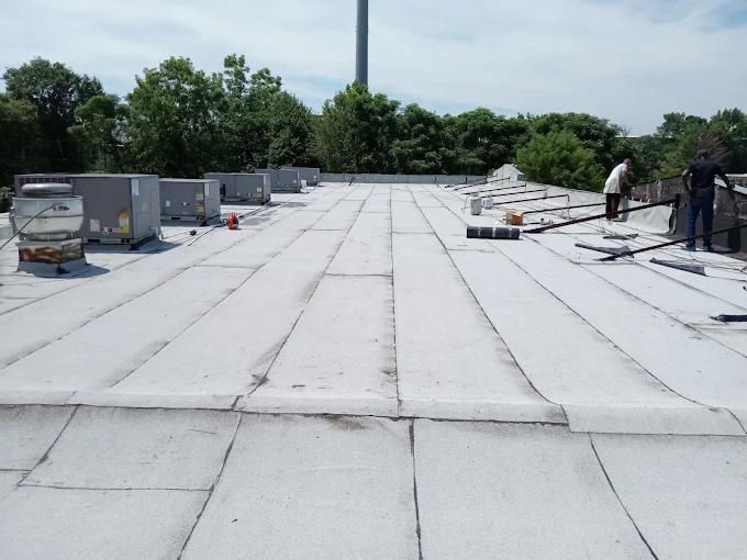 Workers stand on a white flat roof with HVAC units in the background under a blue sky.