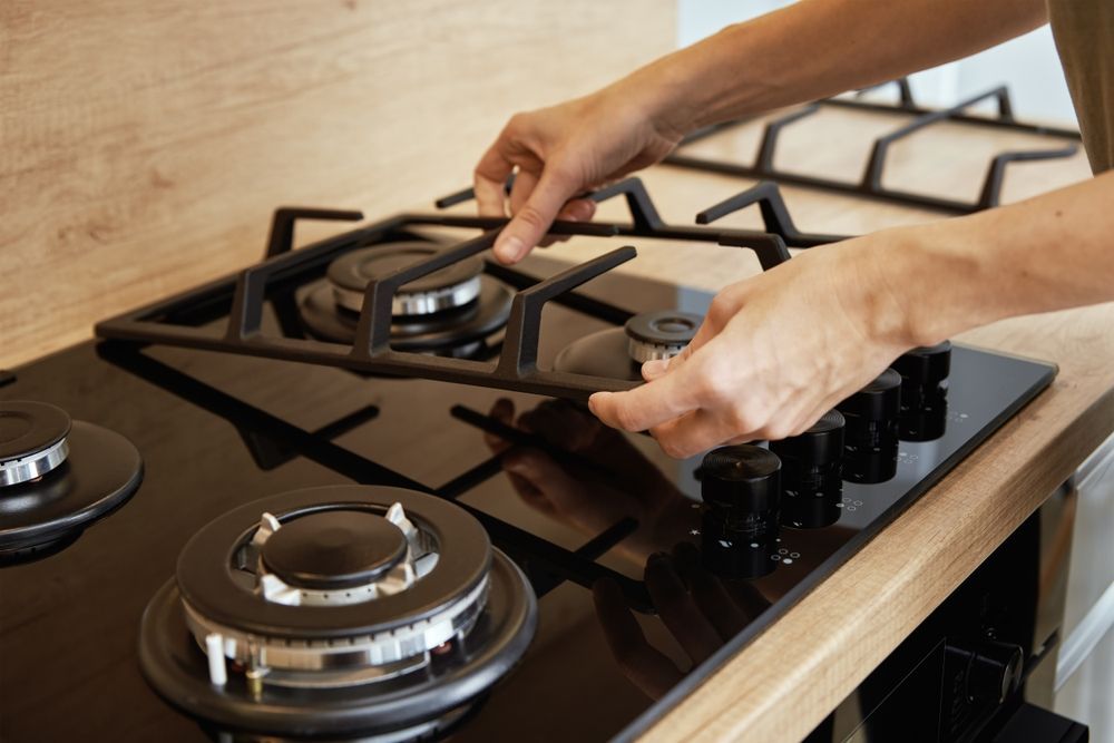 Hands placing a black gas stove grate on a stovetop. Wooden countertop.