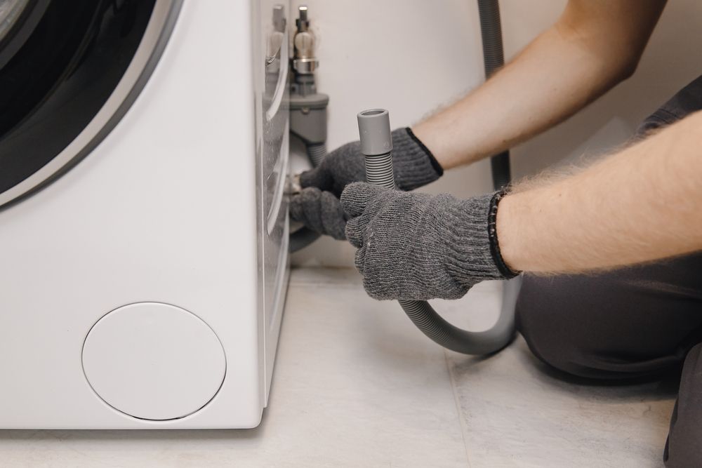 Person connecting a hose to a washing machine in a laundry room.