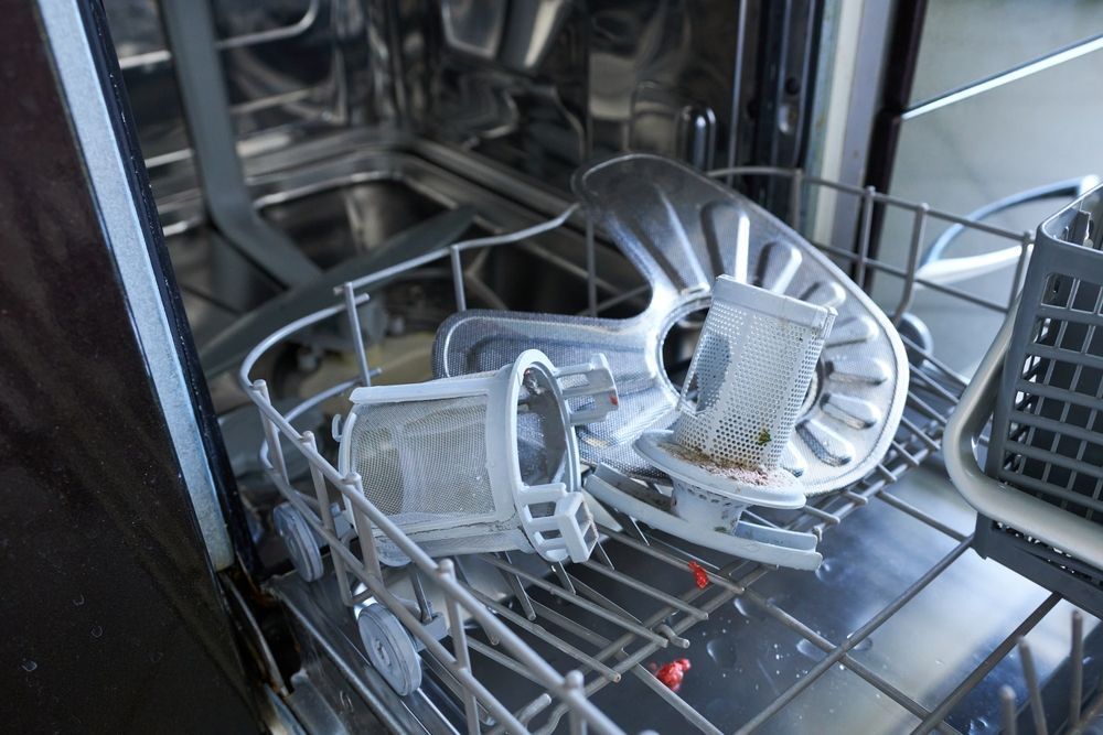Inside a dishwasher, the filter and a spinner arm are disassembled for cleaning.