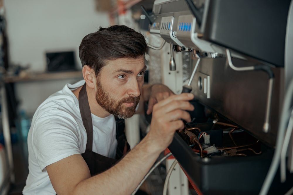 Man fixing an espresso machine with a screwdriver, in a shop setting.