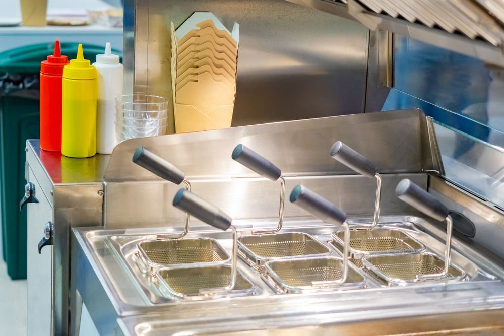 Deep fryers and condiments in a fast-food kitchen. Stainless steel with red, yellow, and white squeeze bottles.