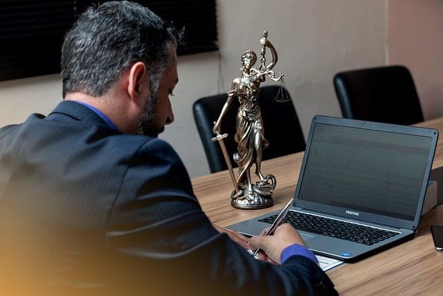 Un hombre está sentado en una mesa con una computadora portátil y una estatua de la justicia.