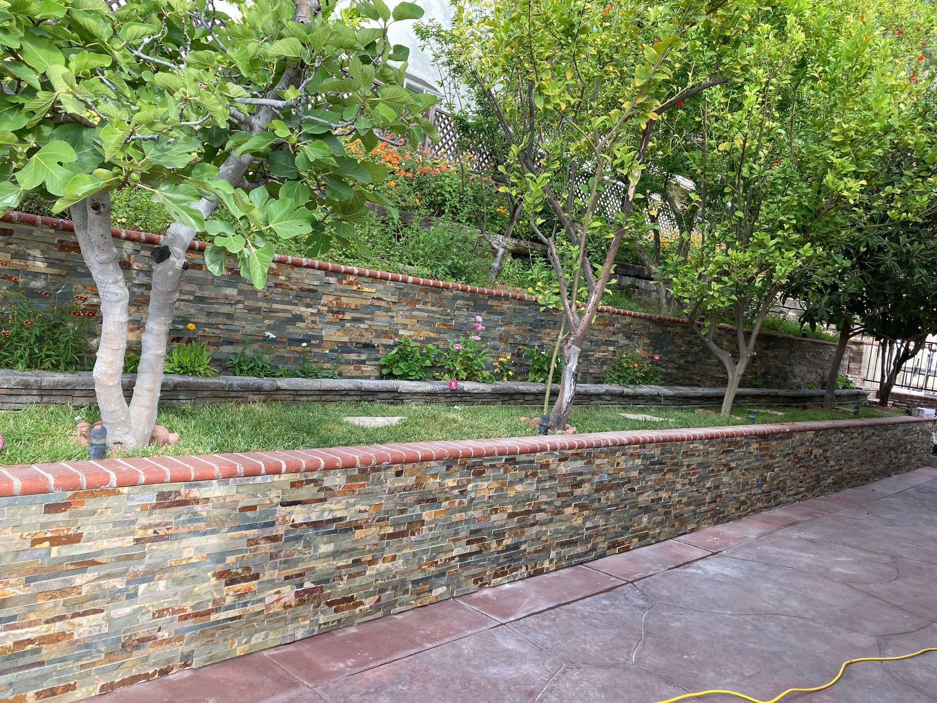 A stone wall with a brick border is surrounded by trees and grass.