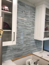 A kitchen with a blue tile wall and white cabinets