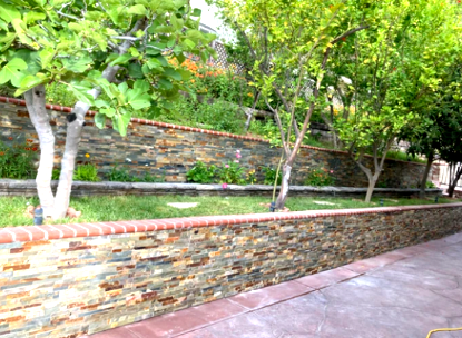 A stone wall surrounds a garden with trees and grass