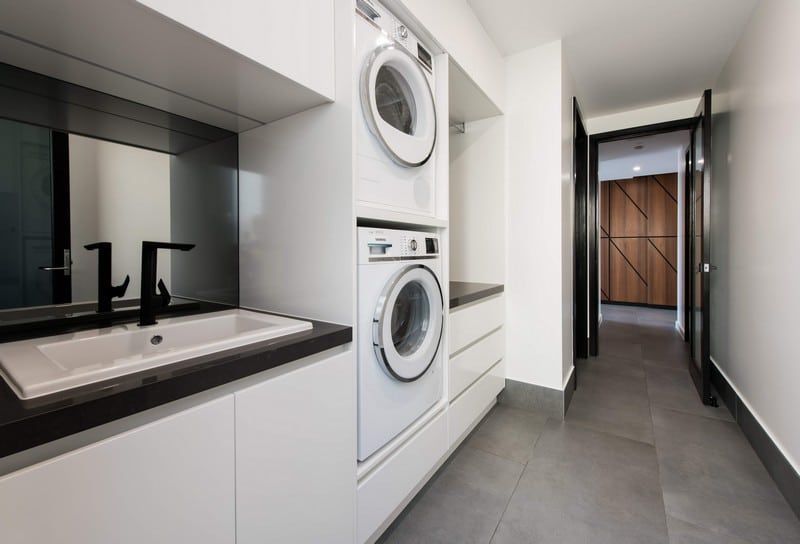 Modern laundry hallway with stacked washer and dryer beside a sink and white cabinets