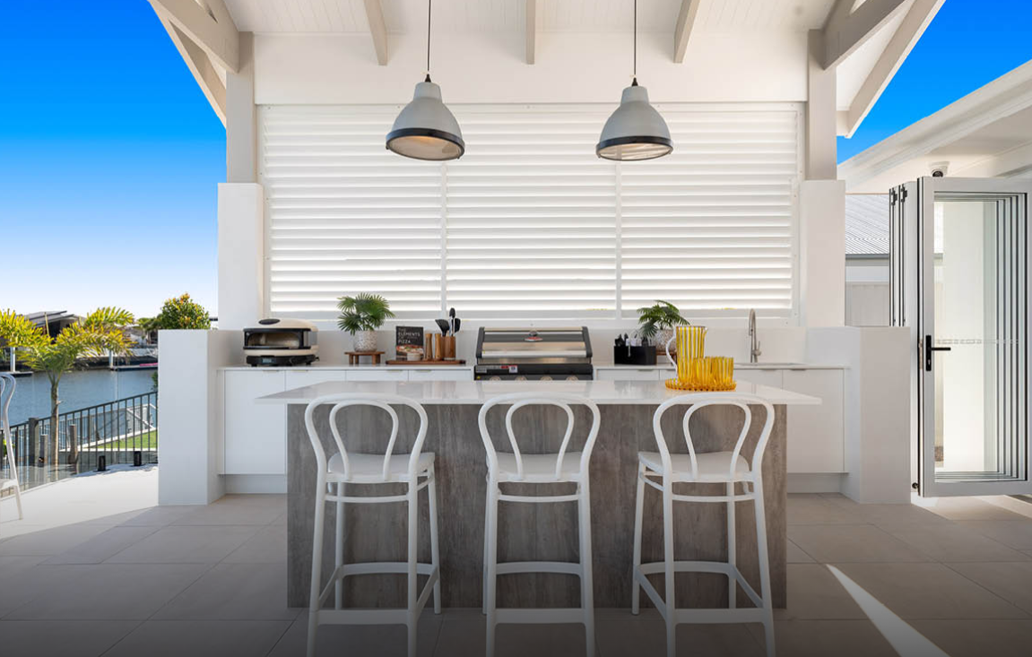 Bright white patio bar with stools, pendant lights, and ocean view through open sliding doors