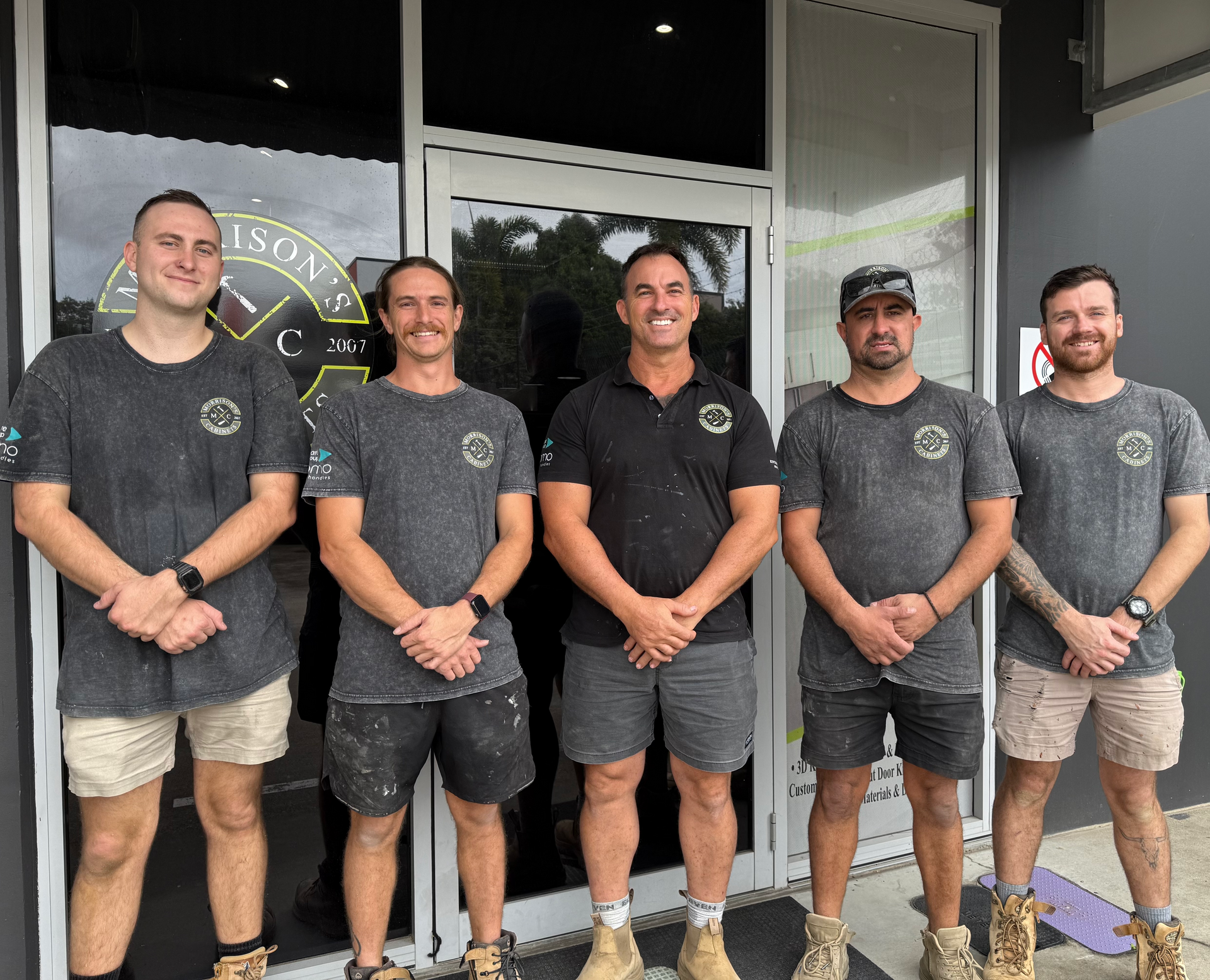 Five staff members in matching gray shirts stand outside a storefront, smiling at the camera.