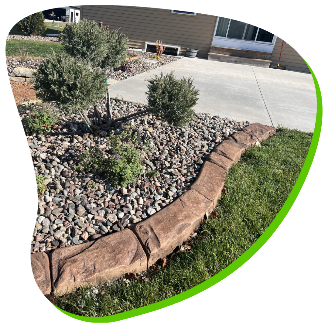 A concrete curb is surrounded by rocks and grass in front of a house.