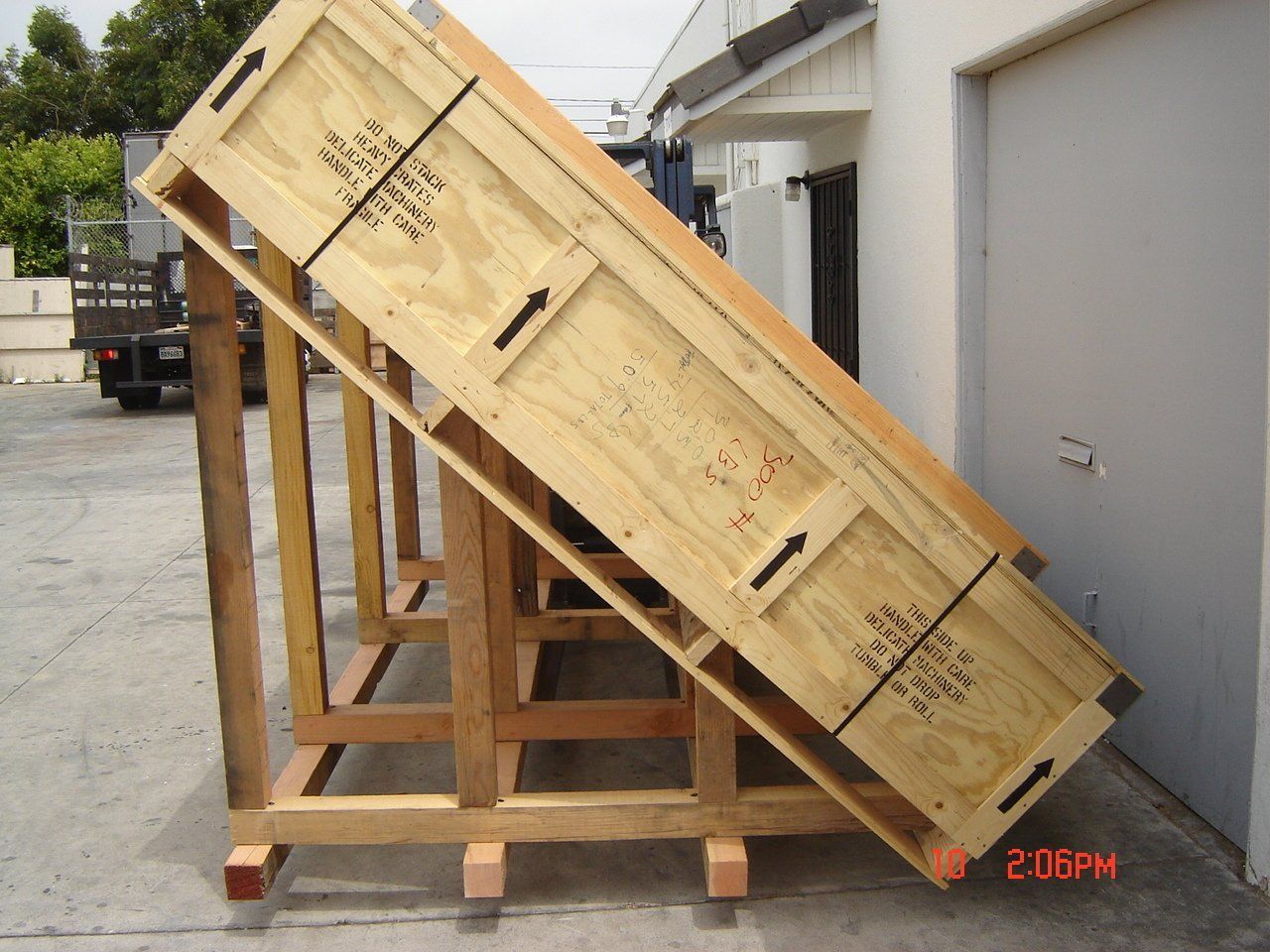Wooden crate on wooden supports, leaning against a building. Black arrows indicate crate direction.