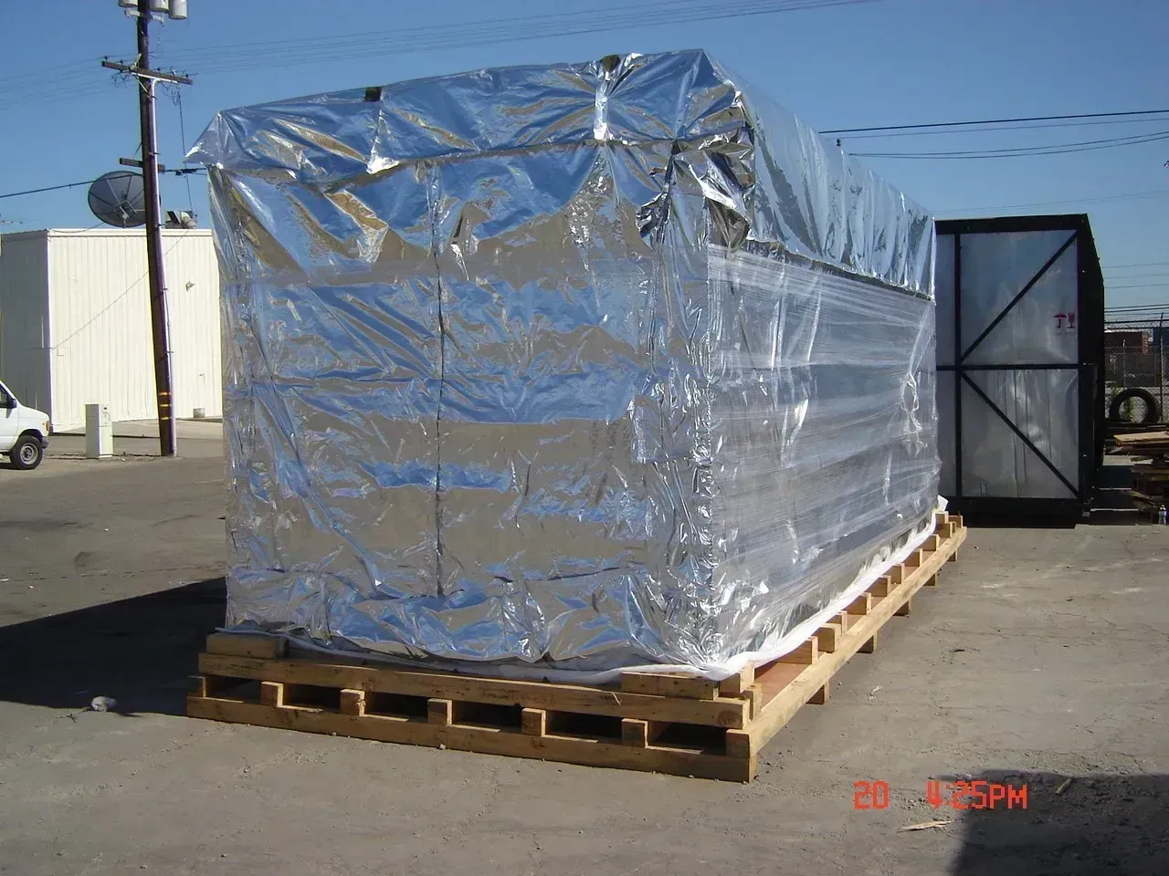 Large, rectangular object wrapped in reflective silver foil on a wooden pallet, outdoors.
