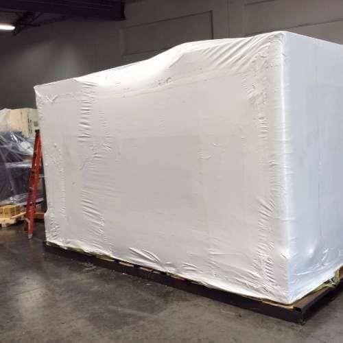 Large white-wrapped object on a pallet in a warehouse. A ladder is visible nearby.