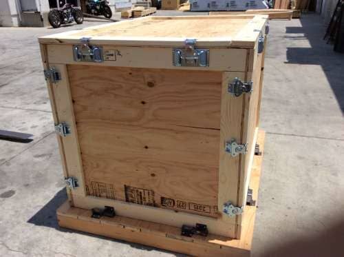 Wooden crate secured with metal hardware, sitting on a wooden pallet outdoors.