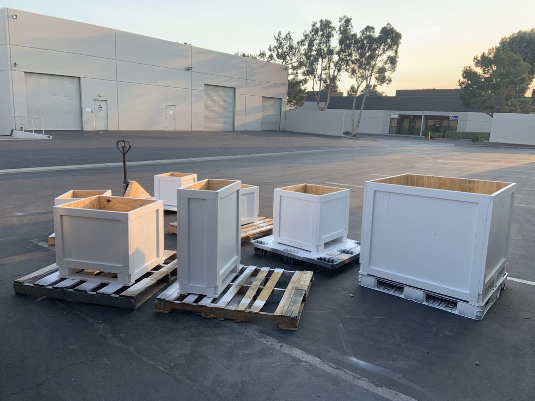 White containers on pallets in an industrial lot. Building in background, sunlight.