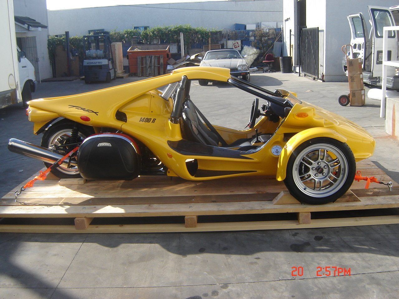 Yellow three-wheeled vehicle on wooden pallet, outdoors.