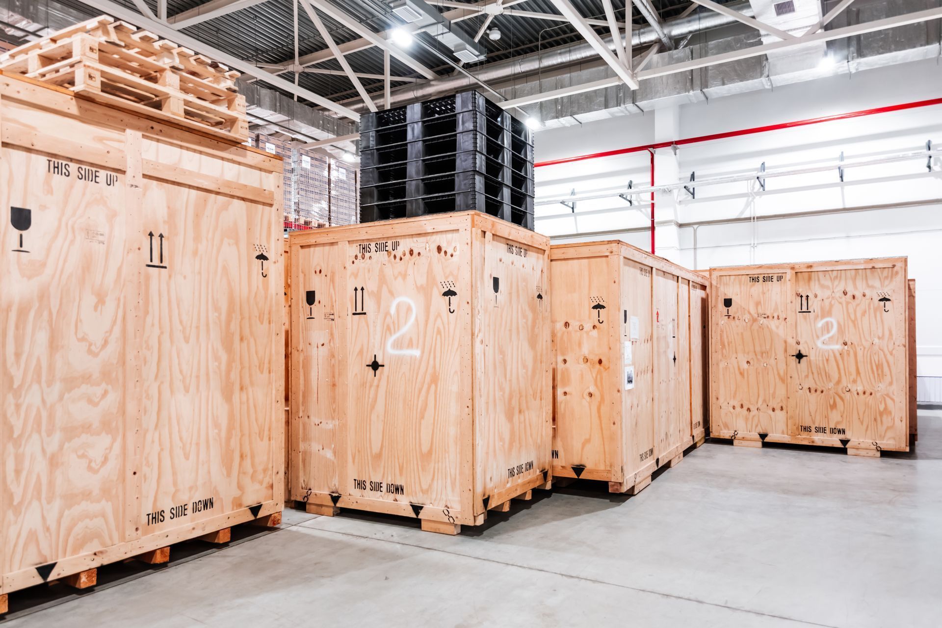 Wooden crates stacked inside a warehouse. Some crates have labels and markings.