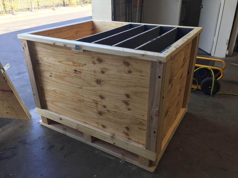 Wooden shipping crate with internal dividers, resting on a pallet outdoors.