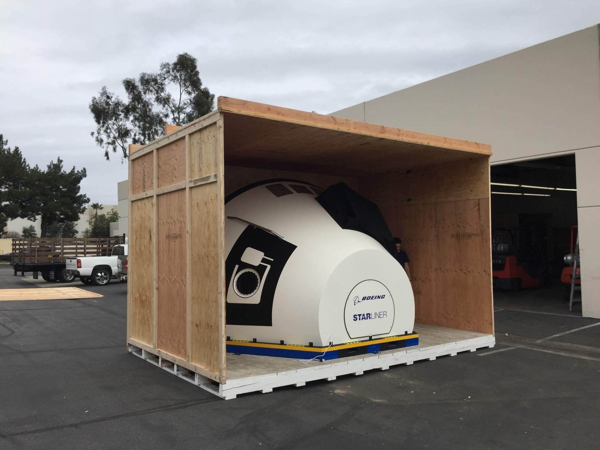 A large, white medical machine is crated in a wooden shipping container, on a loading dock.