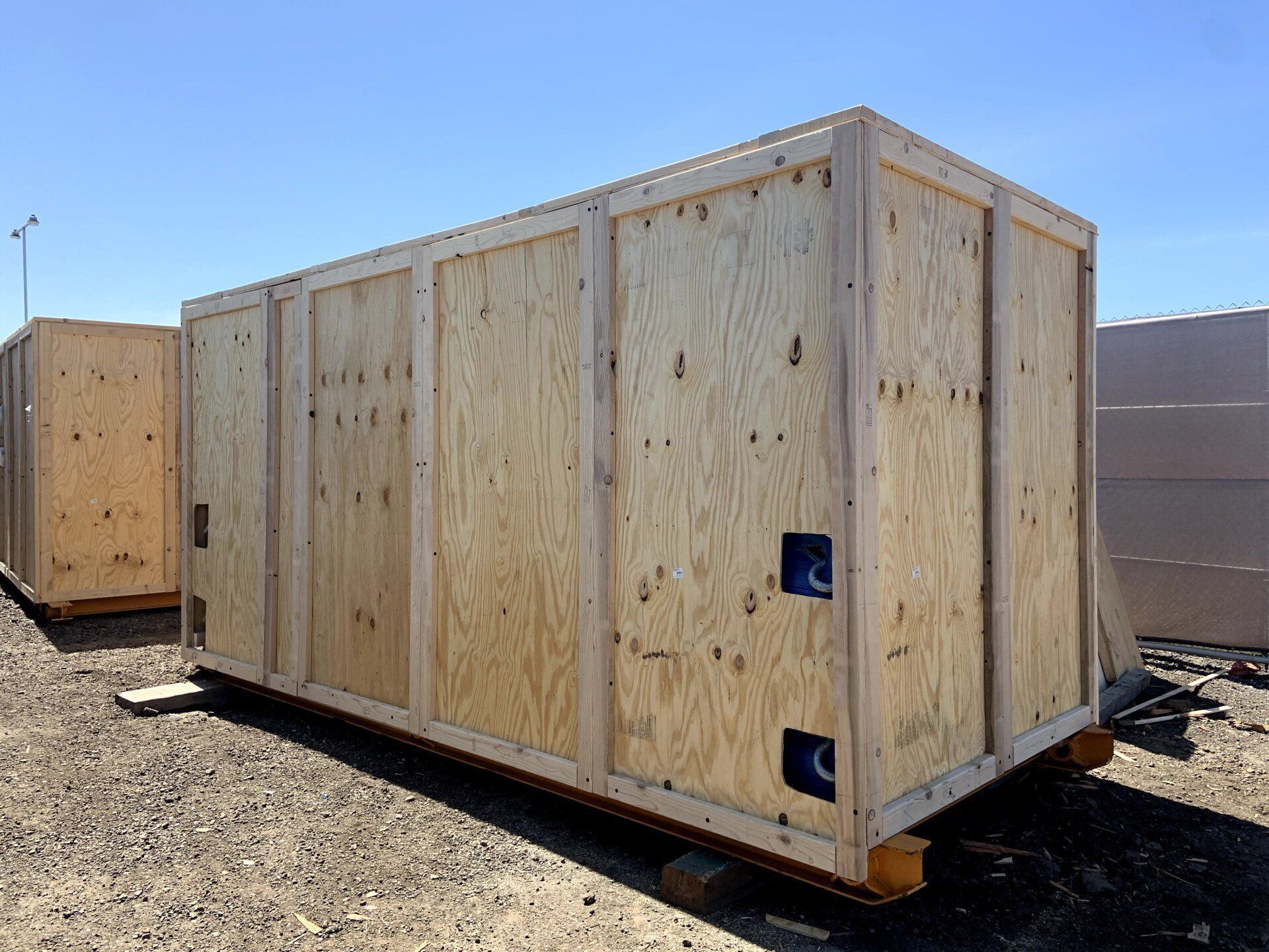 Large wooden shipping crate on a gravel surface under a clear, blue sky.