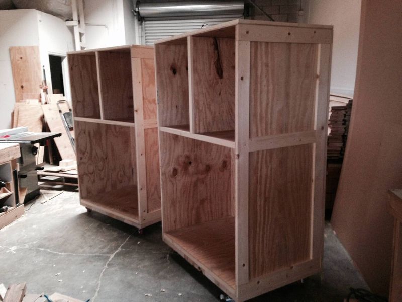 Two unfinished wooden storage cabinets on wheels in a workshop.