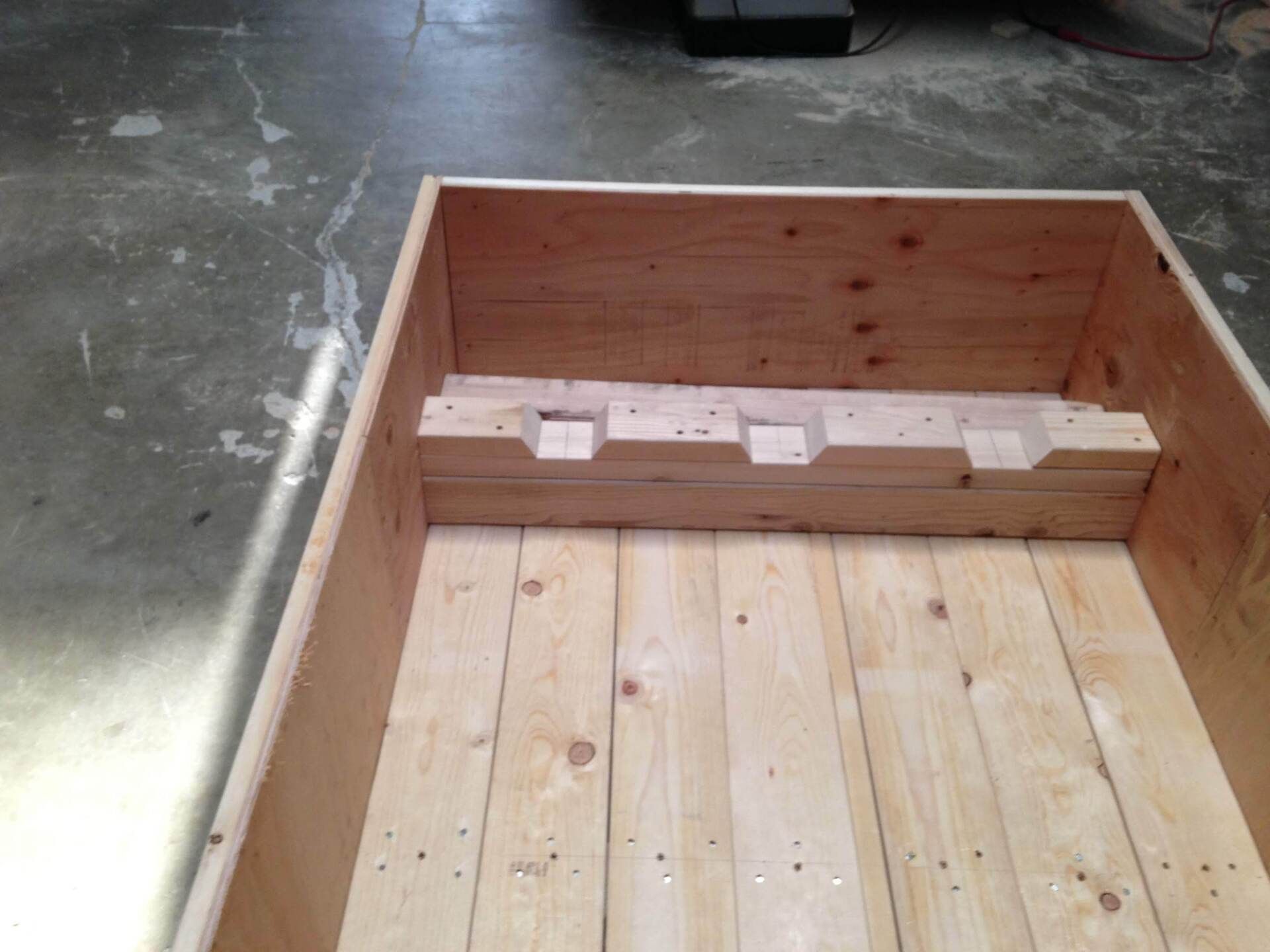 Wooden box with a raised internal platform, constructed of wood planks, on a concrete floor.