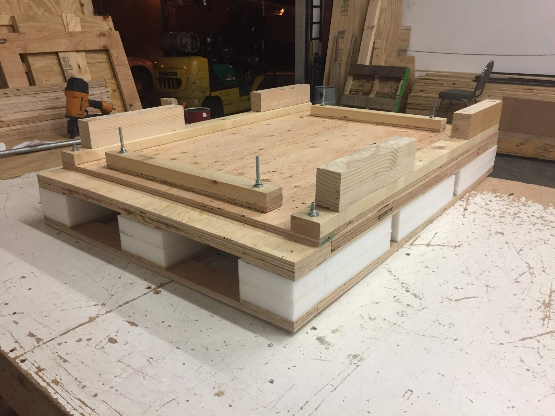 Wooden pallet with foam insulation and built-up top, likely for a shipping container, on a workbench.