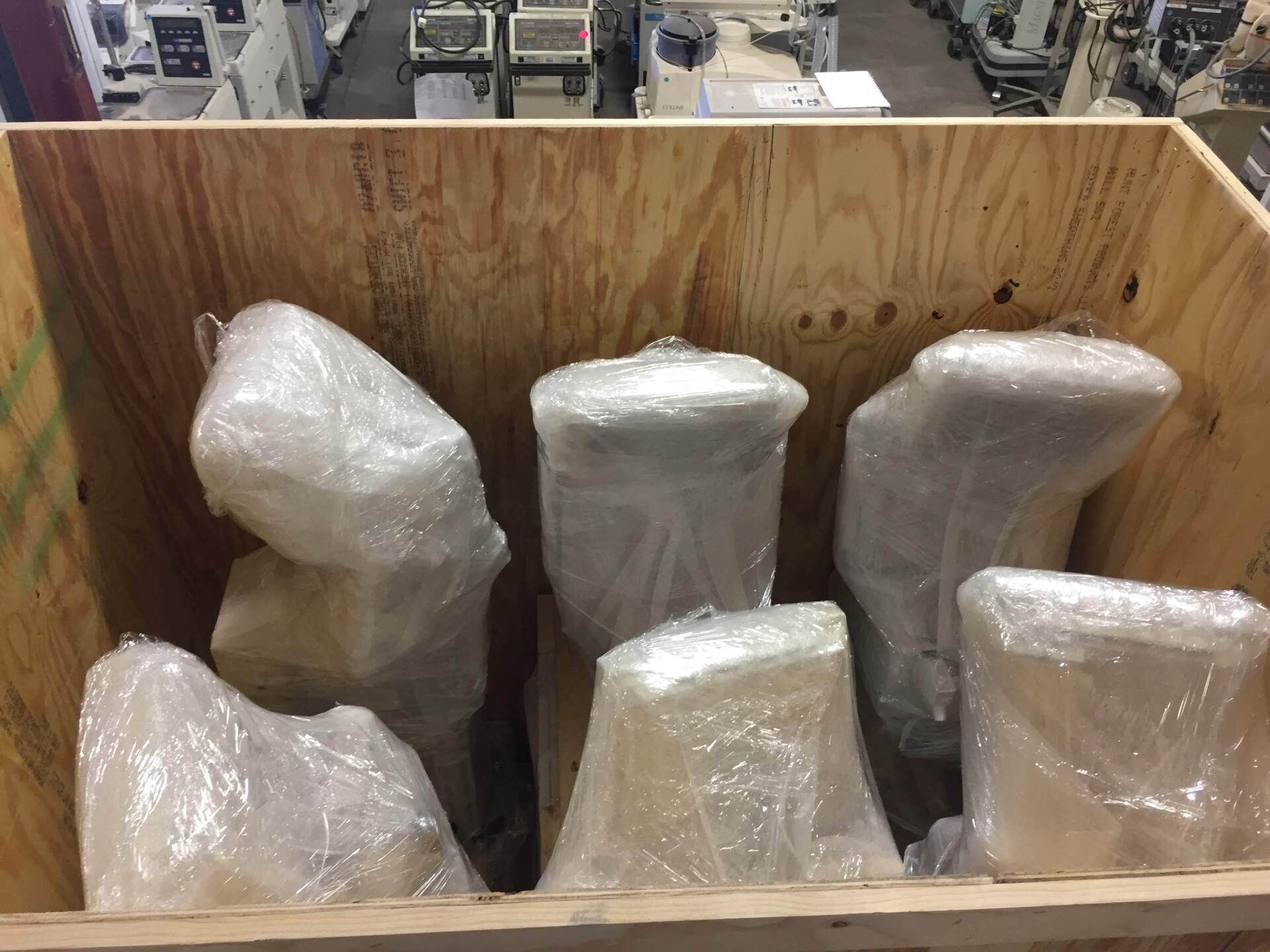 Wooden crate filled with seven items wrapped in clear plastic, possibly machinery parts.