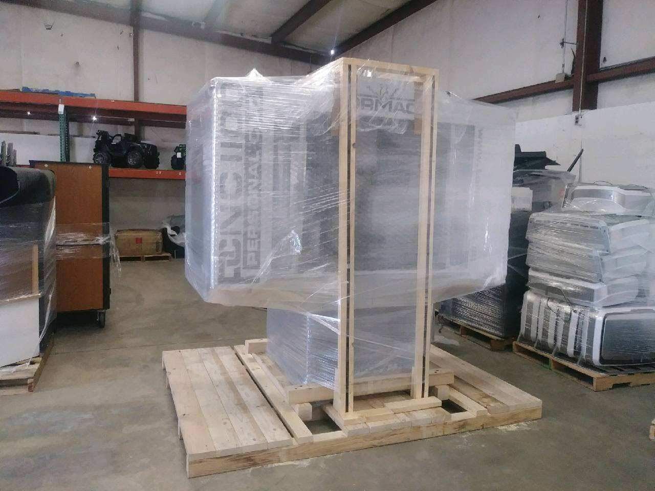 Large machine wrapped in plastic on a wooden pallet inside a warehouse.