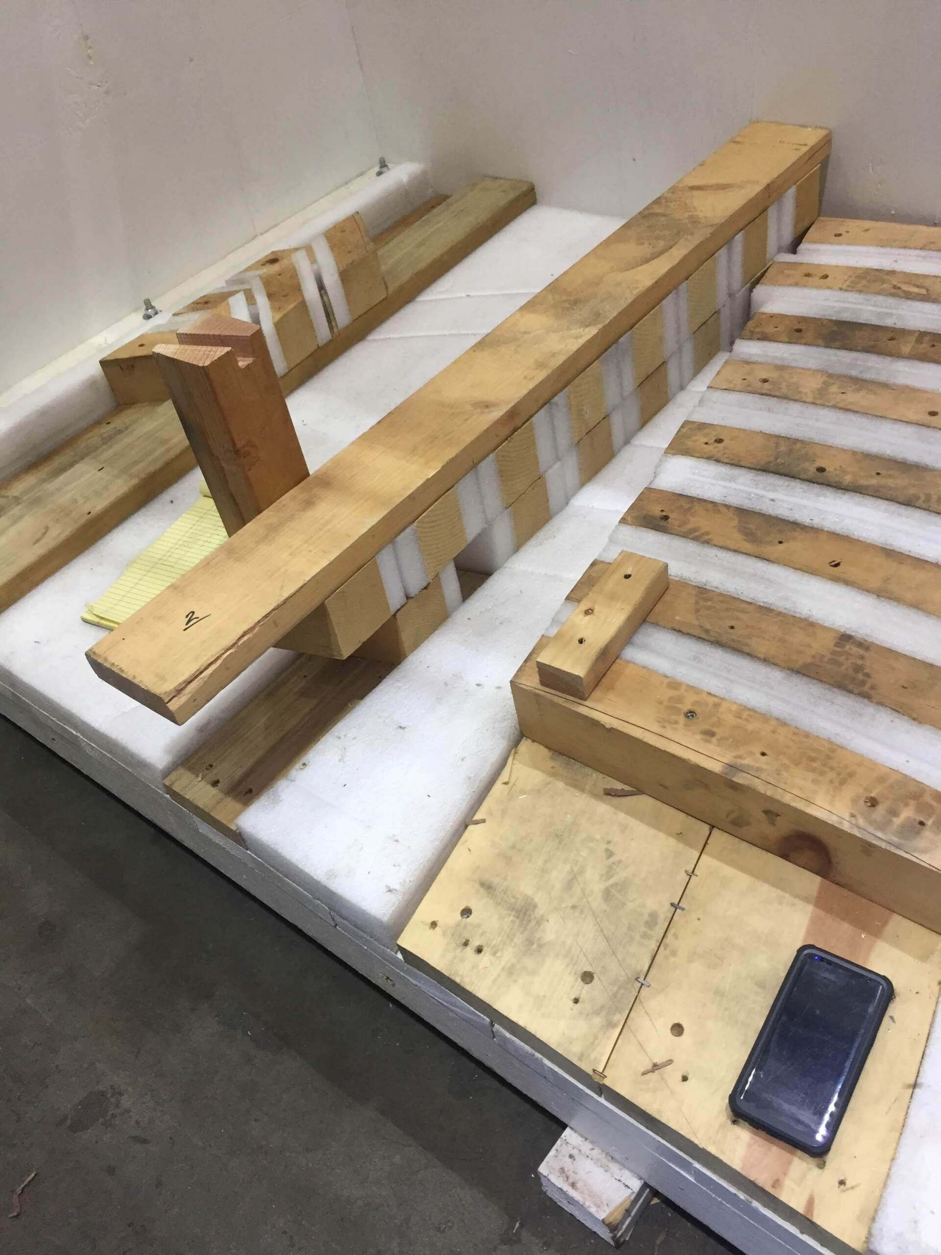 Wooden pallet pieces arranged on a white surface, taped together. A phone rests on one piece.