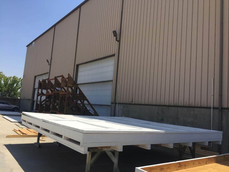 Large white wooden platform on legs in front of a metal building with loading doors.