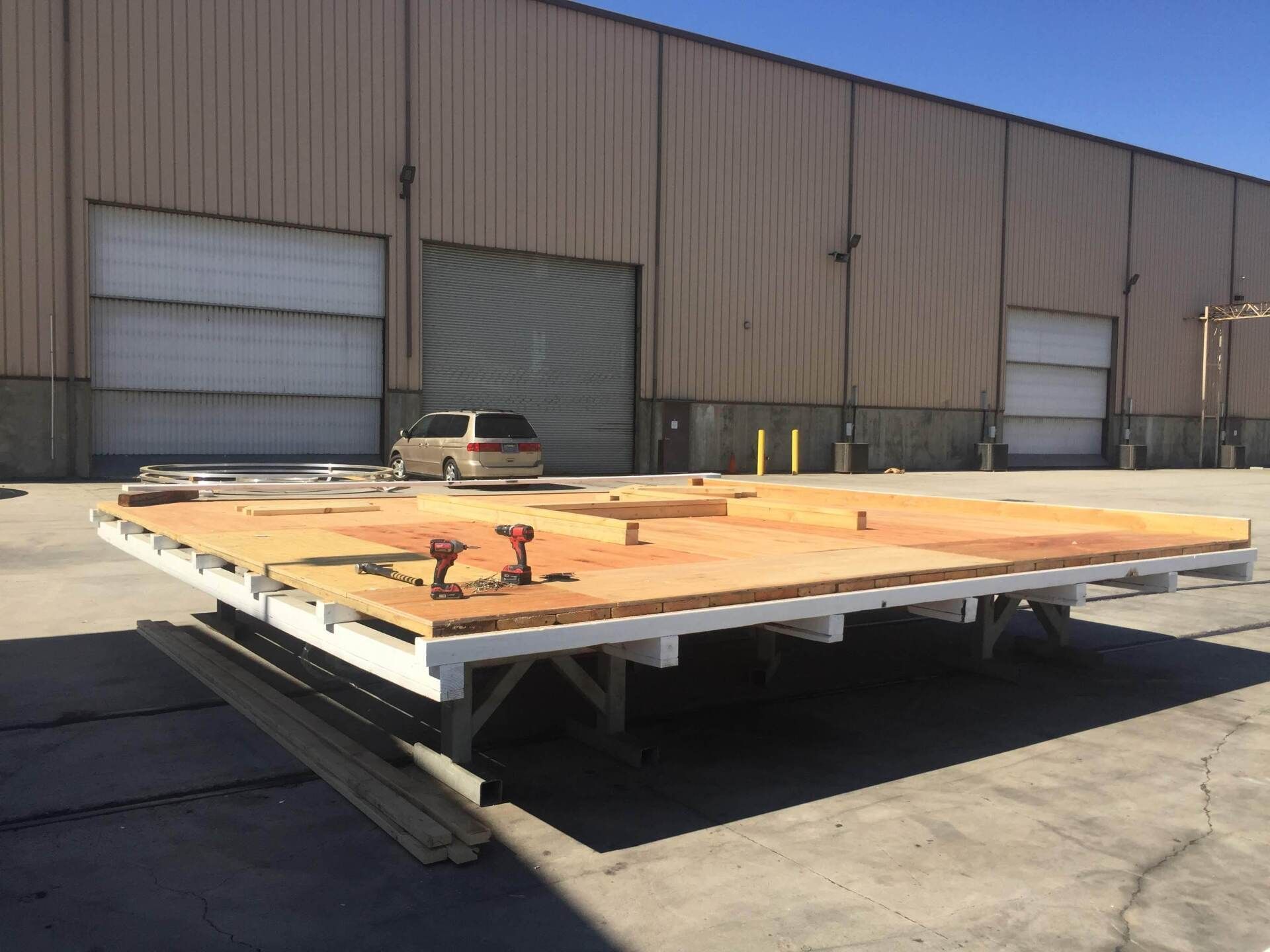 A wooden platform on sawhorses in front of a tan industrial building. Tools are on the platform.