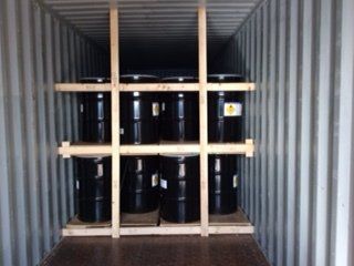Six black barrels inside a shipping container, secured by wooden framing.