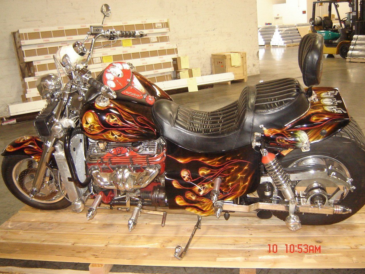 Custom motorcycle with flame and skull artwork, chrome details, resting on wooden pallet.