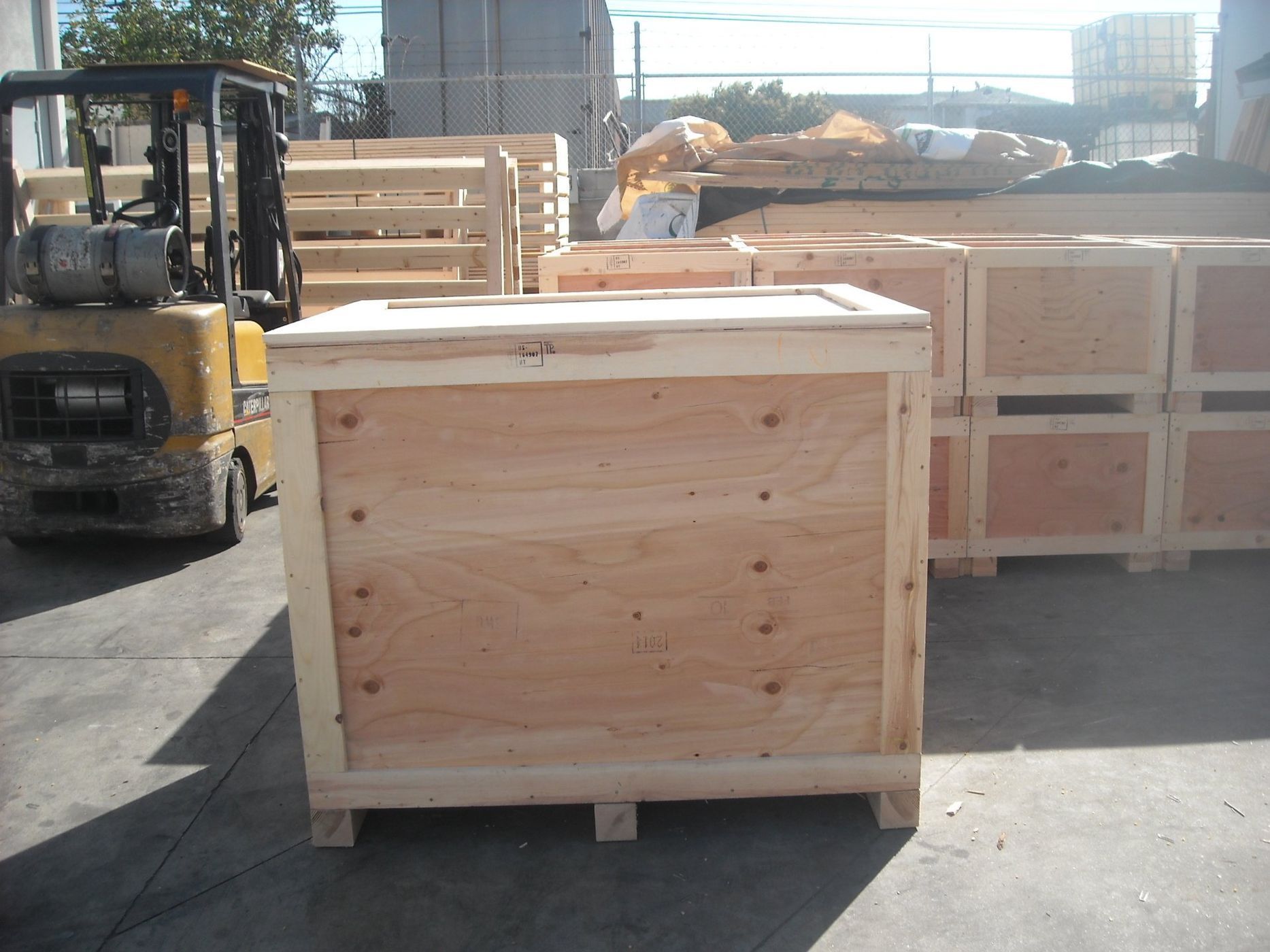 Wooden crate on a pallet in an outdoor industrial setting, a forklift in the background.
