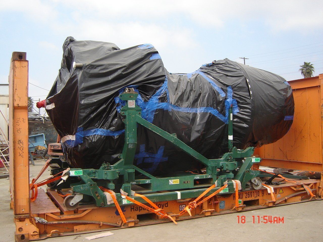 Large black-covered object secured to a green frame inside an orange shipping container.