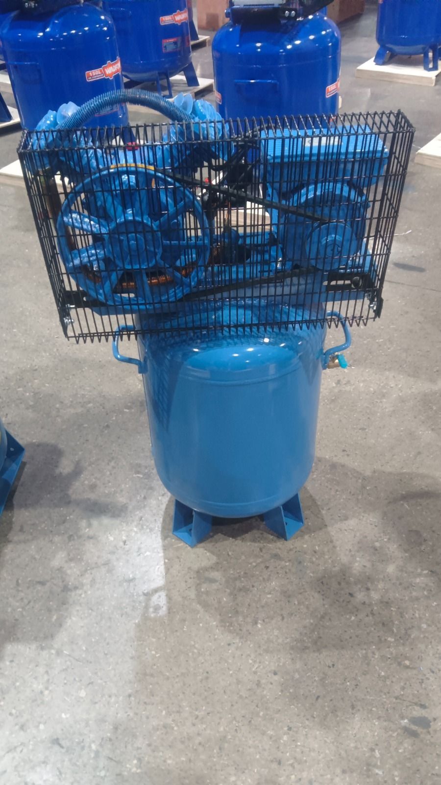 Compresor de aire azul con jaula protectora sobre un piso de concreto.