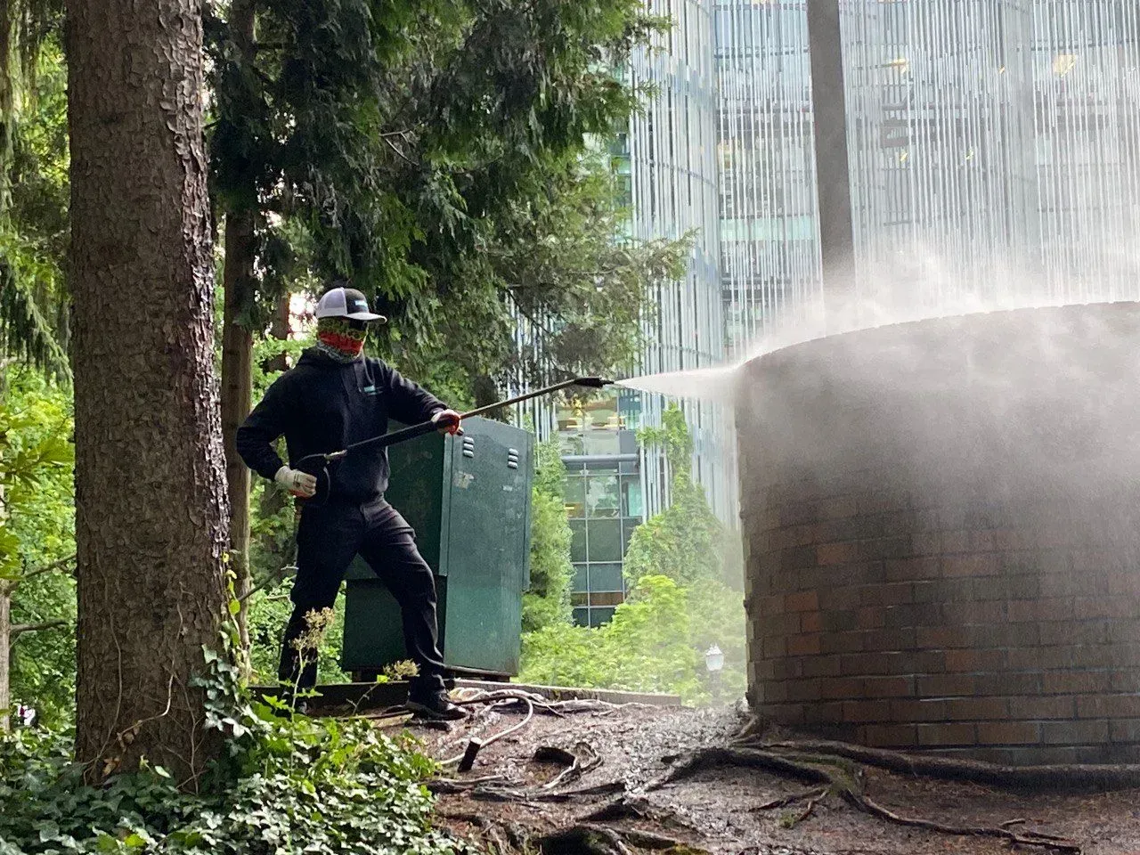 Person power washing a brick structure in a wooded area, creating mist.