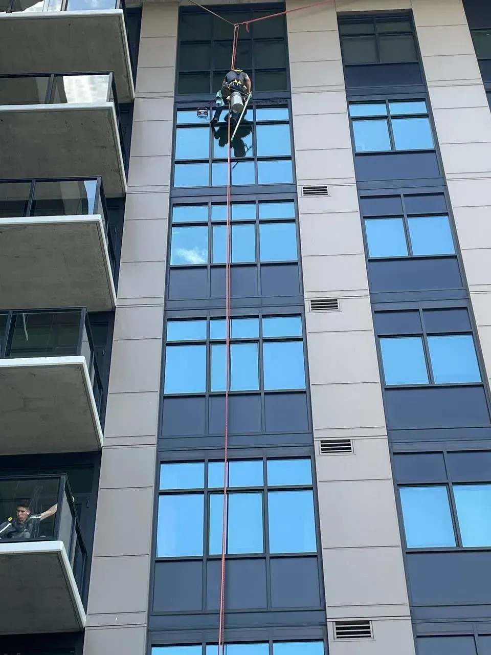 Person rappelling down a high-rise building's windows, secured by a rope.