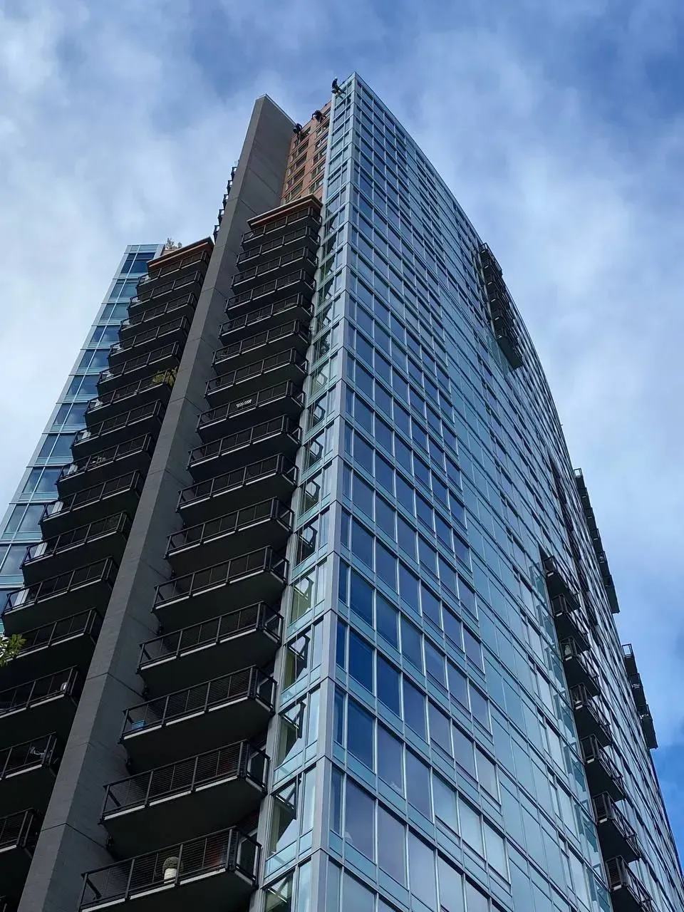Tall, modern glass skyscraper against a cloudy sky, balconies visible on one side.