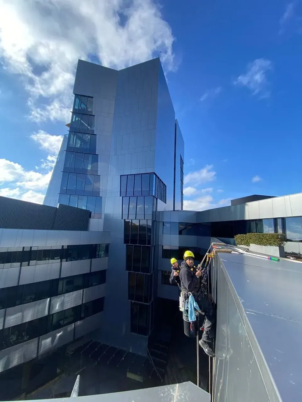 Workers on a building's edge, inspecting the modern architecture. Blue sky and reflective metal surfaces.