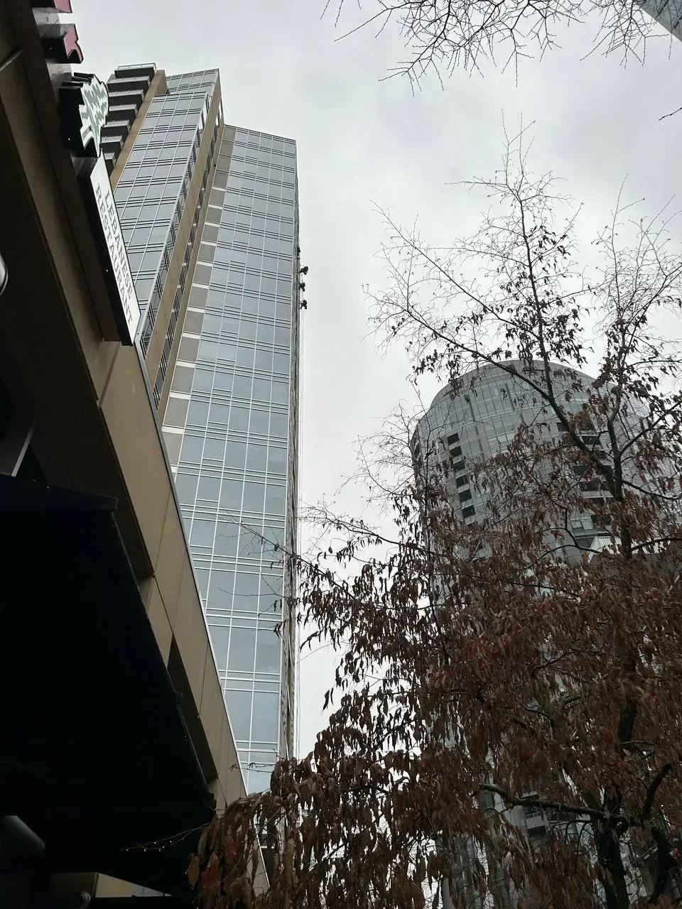 Two tall modern buildings rise on a cloudy day, one with a glass facade, the other with rounded shape.