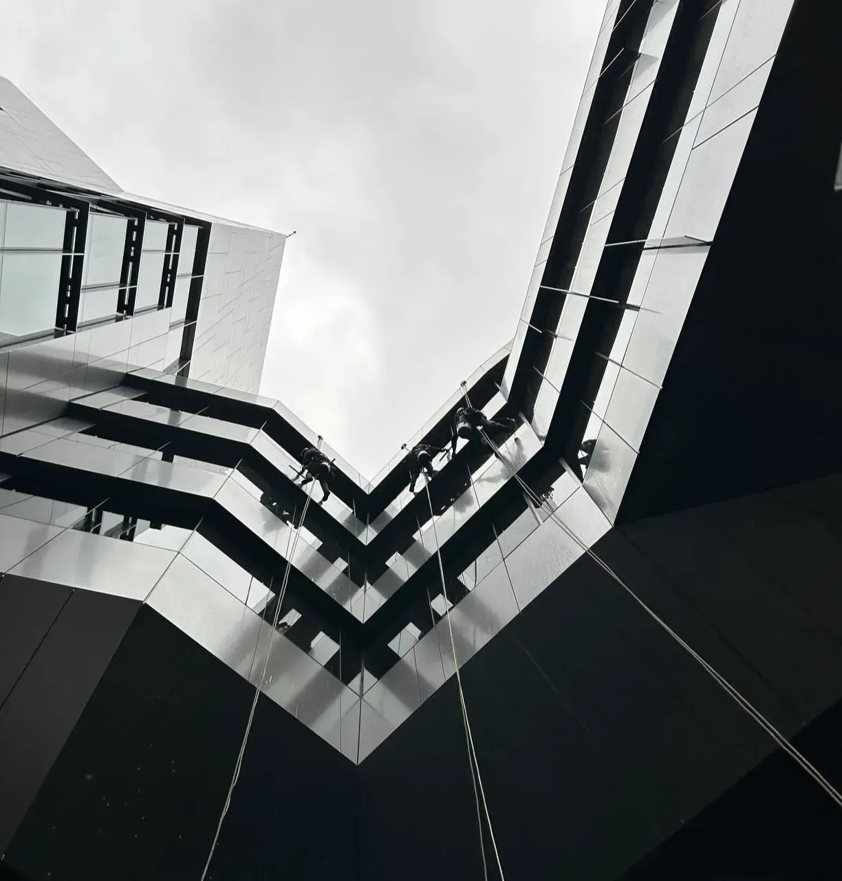 Low-angle view of a modern building with black and silver panels converging towards a cloudy sky.