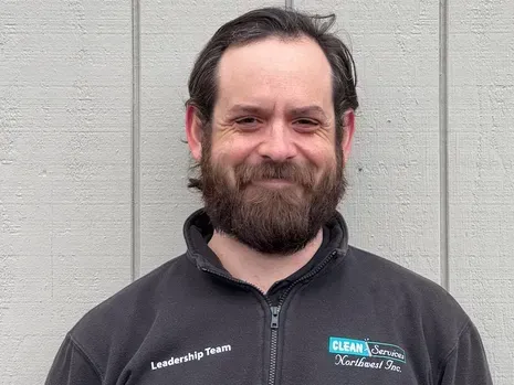 Man with beard in a black jacket smiles in front of a gray wall; Clean Energy Northwest logo visible.