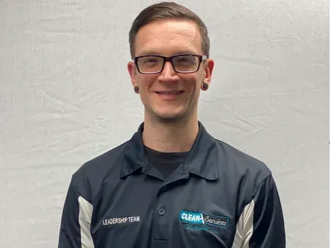 Man wearing glasses, black shirt with logo. Smiling.